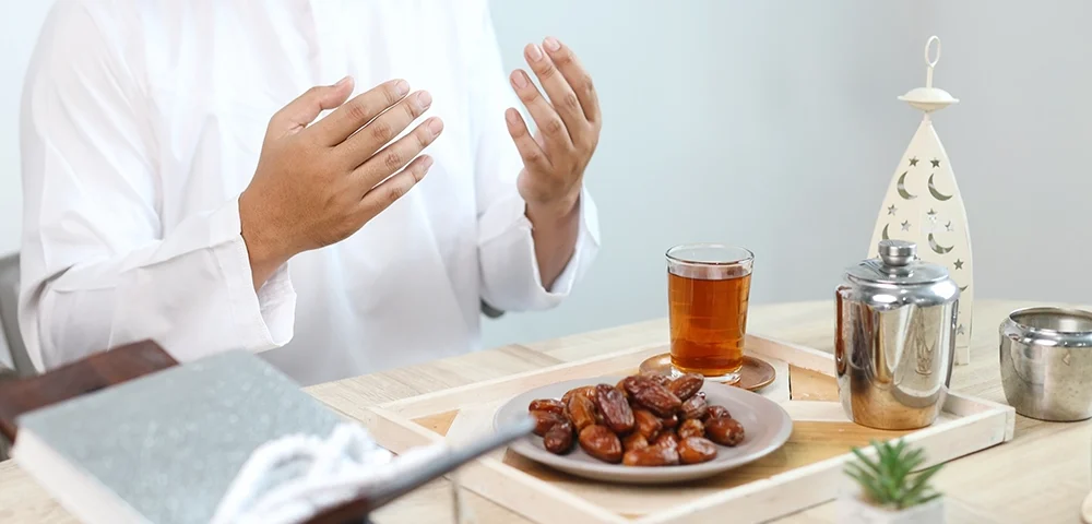 Ramazan ayında iftar öncesinde dua eden Müslüman bir adam, hurma ve çay bulunan sofrada