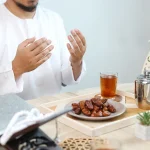 Ramazan ayında iftar öncesinde dua eden Müslüman bir adam, hurma ve çay bulunan sofrada Umreye Gidenler İçin Hurma Tavsiyesi