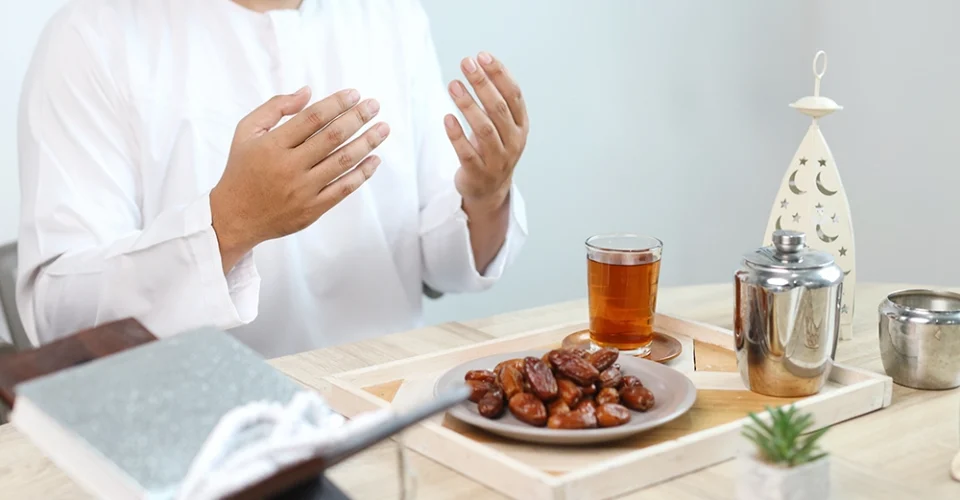 Ramazan ayında iftar öncesinde dua eden Müslüman bir adam, hurma ve çay bulunan sofrada